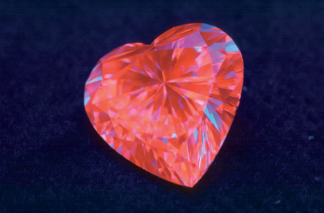 Un diamant taille coeur sous la lumière UV, la lumière qu’il émet n’est pas bleue mais rouge rose.